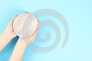 Woman holding silicone implant for breast augmentation on color background, top view with space for text.