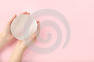 Woman holding silicone implant for breast augmentation on color background, top view with space for text.