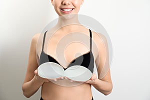 Woman holding silicone implants for breast augmentation on white background, closeup.