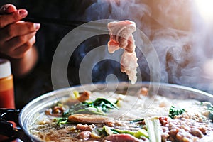 Woman holding sliced beef meat by chopsticks shabu shabu is Korean or Japanese style beef in hot pot dish of thinly sliced meat