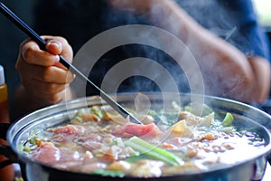 Woman holding sliced beef meat by chopsticks shabu shabu is Korean or Japanese style beef in hot pot dish of thinly sliced meat an