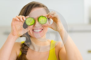 Woman holding slices of cucumber in front of eyes