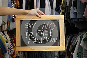 Woman holding small chalkboard with phrase SAY NO TO FAST FASHION in clothes store, closeup