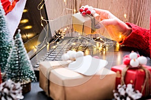Woman holding small present box in hand and using search by laptop. Christmas Concept. Online shopping. Holiday sale