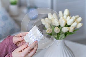 Woman holding small white gift box and greeting card with bouquet of white tulips flowers on valentines day.