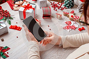 Woman holding smart phone with blank screen for mockup, surrounded by Christmas and New Year decorations