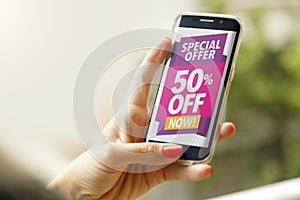 Woman holding a smartphone with a 50% discount advertising on the screen.