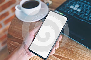 Woman holding smartphone with blank white screen on wooden table at coffee shop.Blank screen mobile phone for graphic display