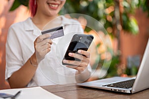 A woman holding a smartphone and a credit or debit card, making an online payment, shopping online