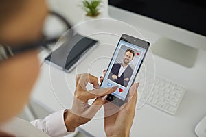 Woman holding a smartphone and looking at a young man's photo on an online dating app