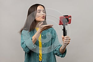 Woman holding smartphone on steadycam, broadcasting livestream or making selfie, sending air kiss.
