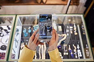 Woman holding smartphone and taking photos of jewelry display