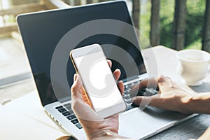 Woman holding smartphone and using laptop