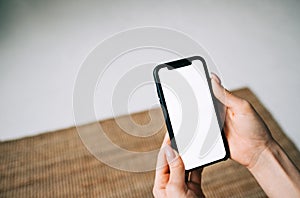 Woman holding a smartphone with a white screen mock up, in living room at home