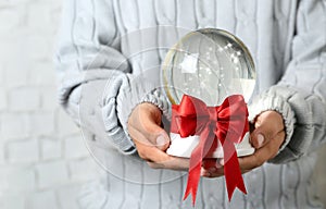 Woman holding snow globe with red bow on blurred background