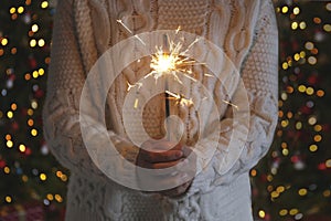 Woman holding sparkler in hands on background of Christmas tree and gifts