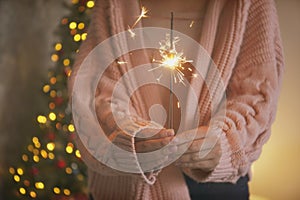 Woman holding sparkler in hands on background of Christmas tree and gifts