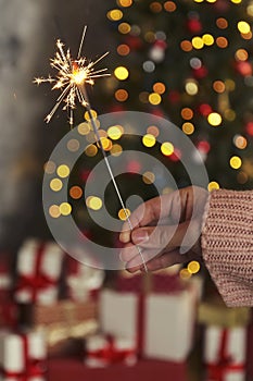 Woman holding sparkler in hands on background of Christmas tree and gifts