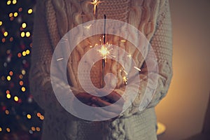 Woman holding sparkler in hands on background of Christmas tree and gifts