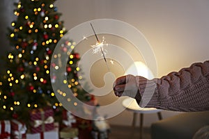 Woman holding sparkler in hands on background of Christmas tree and gifts