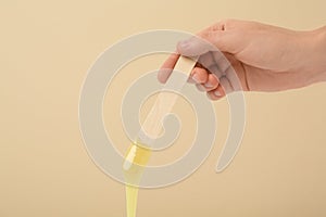 Woman holding spatula with hot depilatory wax on beige background, closeup