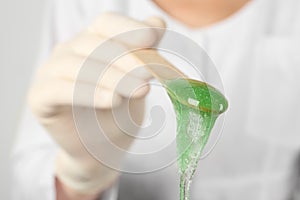 Woman holding spatula with hot depilatory wax, closeup