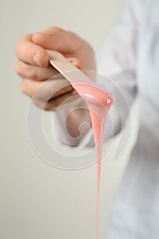 Woman holding spatula with hot depilatory wax, closeup