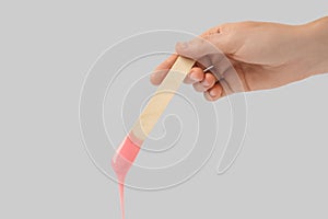 Woman holding spatula with hot depilatory wax on light  background, closeup