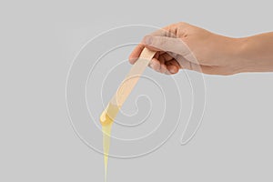 Woman holding spatula with hot depilatory wax on light  background, closeup