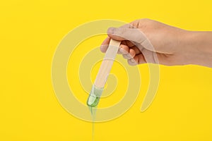 Woman holding spatula with hot depilatory wax on yellow background, closeup