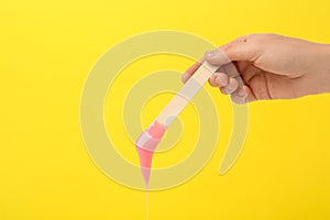 Woman holding spatula with hot depilatory wax on yellow background, closeup