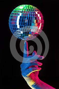 Woman holding spinning disco mirror ball on finger under neon. Glossy silver sphere reflecting light. Retro night party