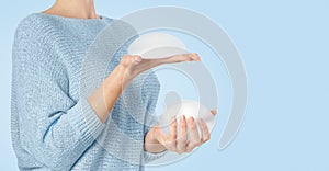 Woman holding and squeezing round implants on blue background. Mammoplasty and plastic surgery.