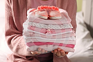 Woman holding stack of baby girl`s clothes with shoes indoors, closeup