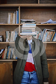 A woman is holding a stack of books in front of a shelf
