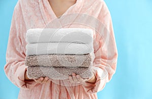 Woman holding stack of fresh clean towels on blue background, closeup