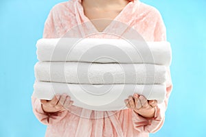 Woman holding stack of fresh clean towels on light blue background, closeup