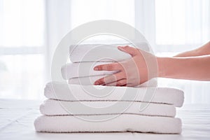 Woman holding stack of white clean bath towels in bedroom interior, copy space. Close up hands of hotel maid with towels.