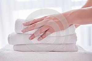 Woman holding stack of white clean bath towels in bedroom interior, copy space. Close up hands of hotel maid with towels.