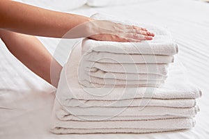 Woman holding stack of white clean bath towels in bedroom interior, copy space. Close up hands of hotel maid with towels.