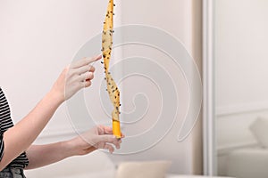 Woman holding sticky insect tape with dead flies indoors, closeup. Space for text