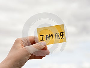 A woman holding a sticky note with the words I AM FREE over a overcast sky background