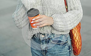 woman holding a string bag and paper cup of coffee