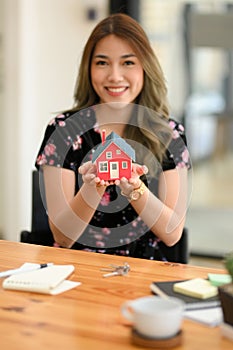 Woman holding a stylish house model over office desk. Residential investment