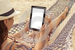 Woman holding a tablet computer with blank screen while lying in a hammock on the beach