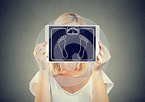 Woman holding tablet weight scale in front of her face