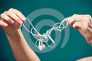 Woman holding tangled earphone trying to untangle it. People and technology concept