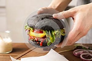Woman holding tasty black vegetarian burger over table