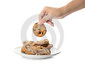 Woman holding tasty chocolate chip cookie over plate on white background