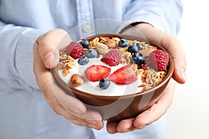 Woman holding tasty homemade granola with yogurt and berries in bowl. Healthy breakfast